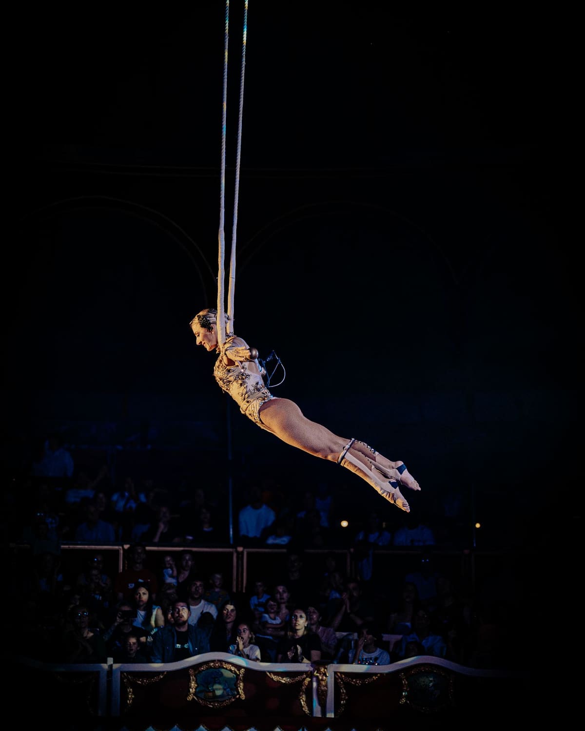 An aerial acrobat suspended above a rapt circus audience