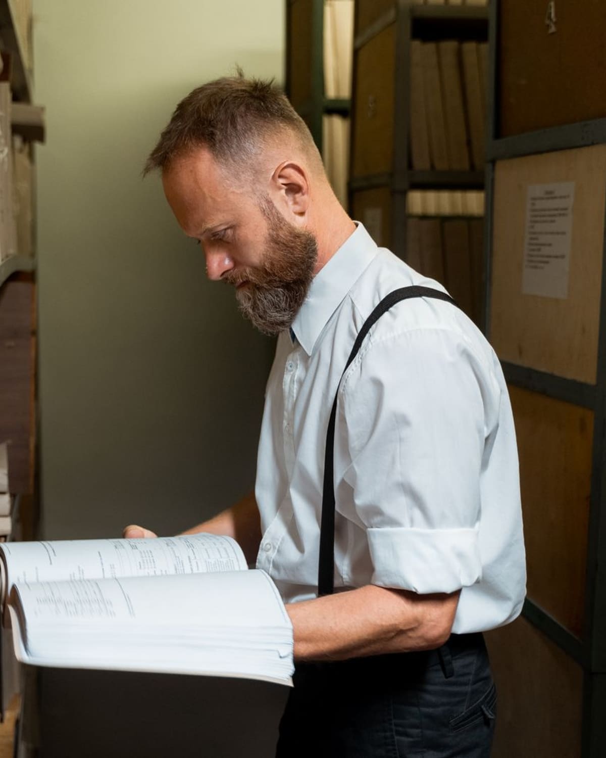 An archivist examining a large bound record among the shelves of an archive