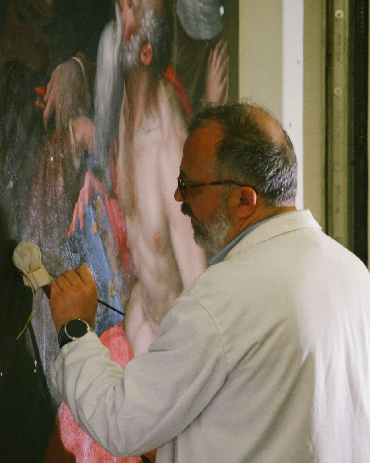 An art conservator in a white coat retouching an old master painting with a fine brush