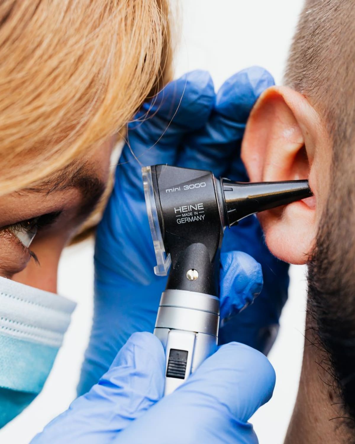 An audiologist examines a patient's ear closely with an otoscope.
