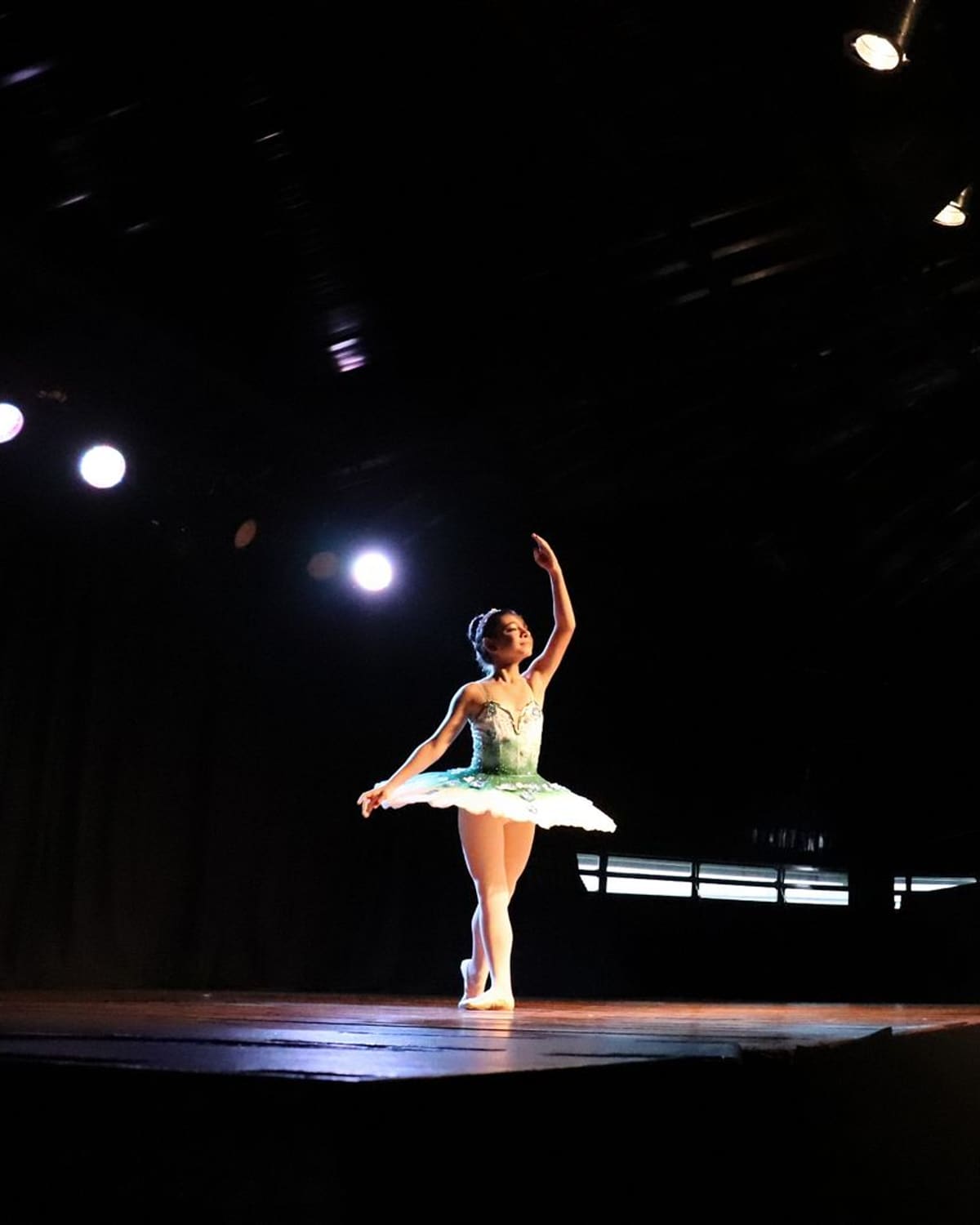 A ballet dancer on pointe under a spotlight on a dark stage