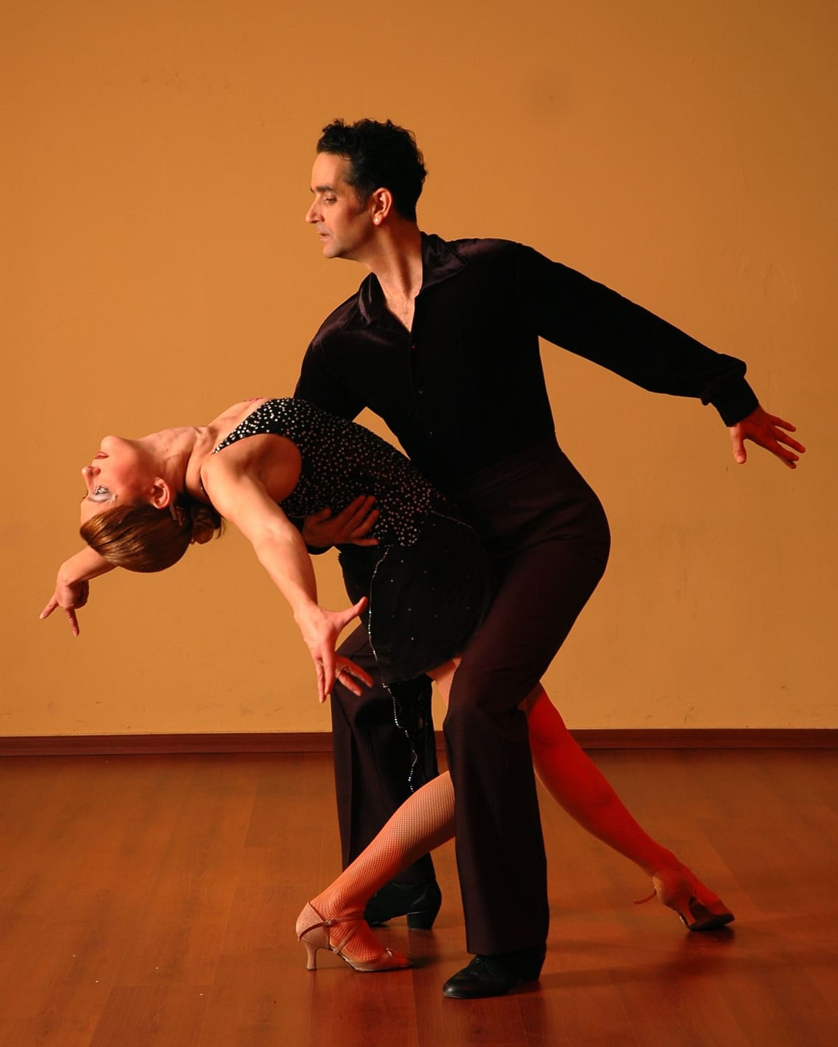 A ballroom couple move together, the man supporting his partner in a deep back-bend.