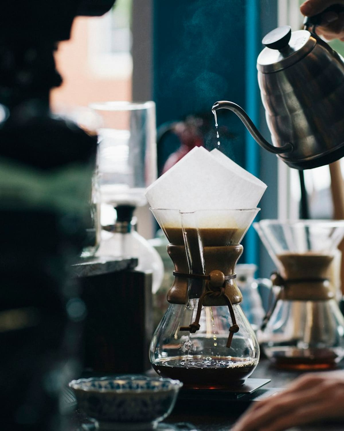 A barista's hand pouring a slow kettle over a filter
