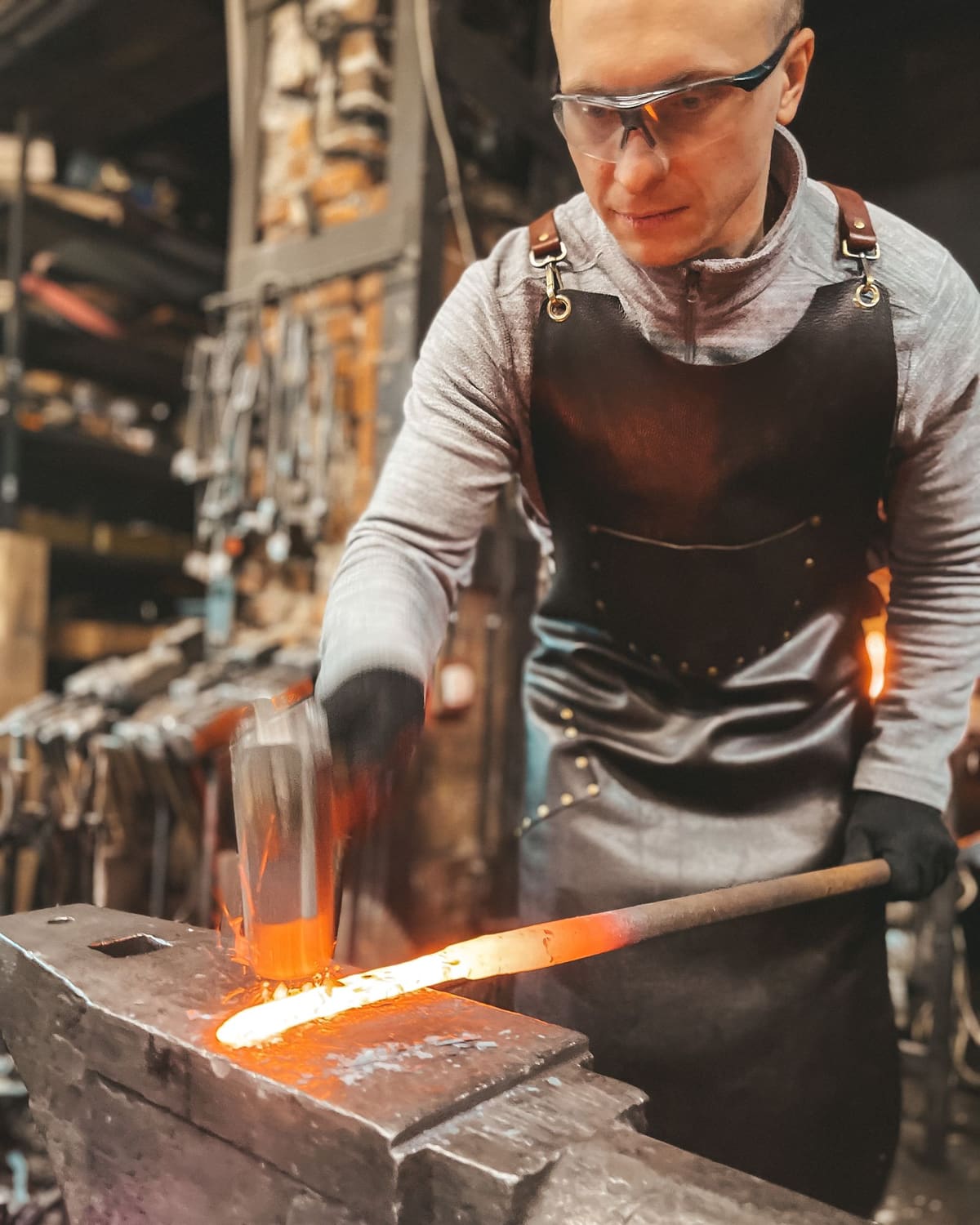 A bladesmith hammering a glowing steel bar on an anvil in a forge