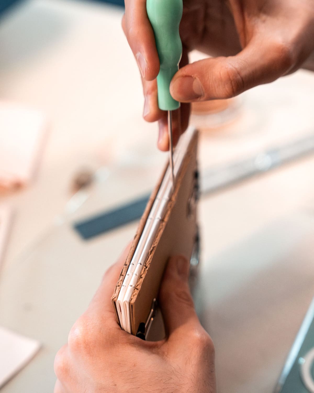 A bookbinder's hands piercing the spine of a book to sew its pages