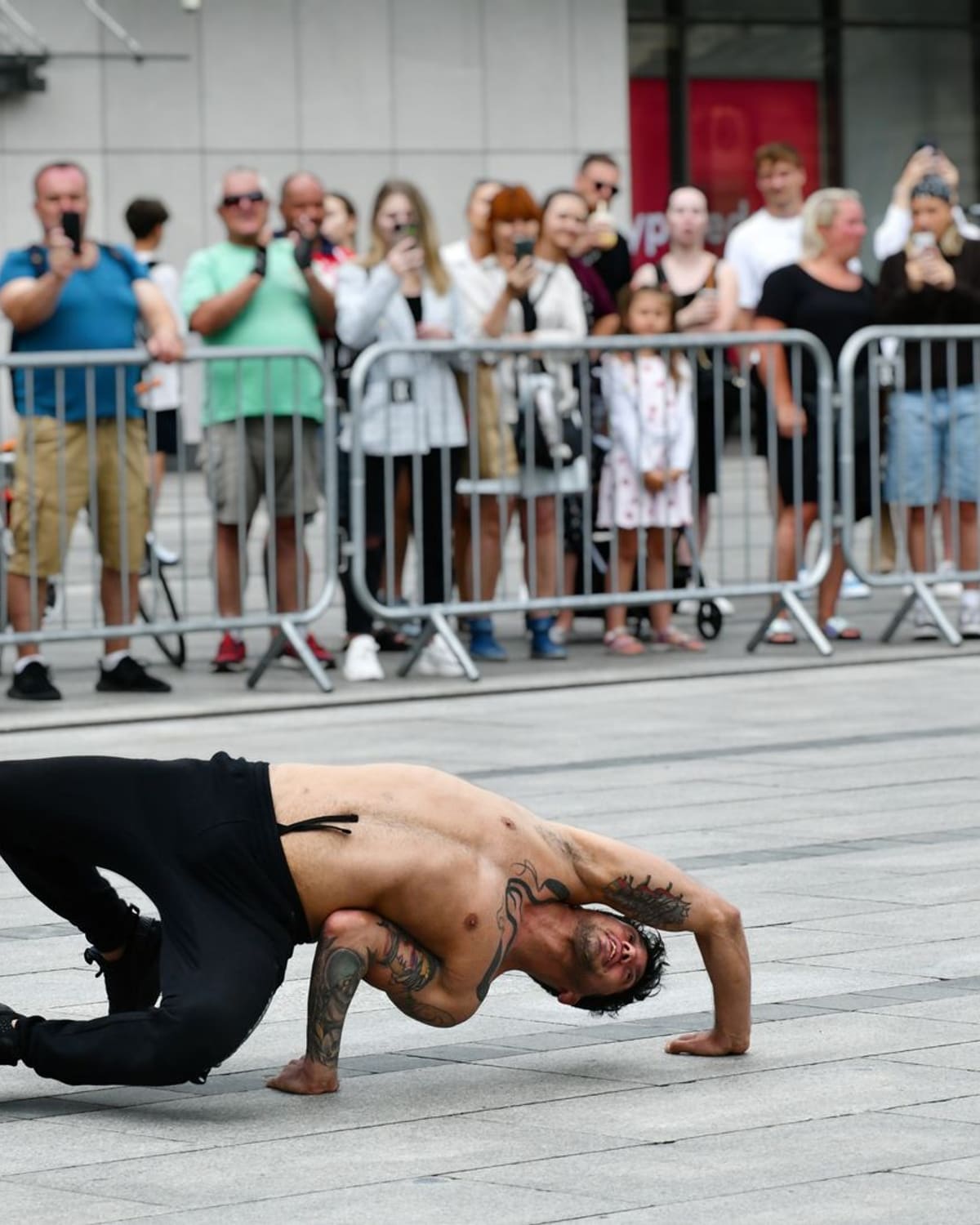 A breakdancer holds a freeze on the pavement in front of a street crowd.