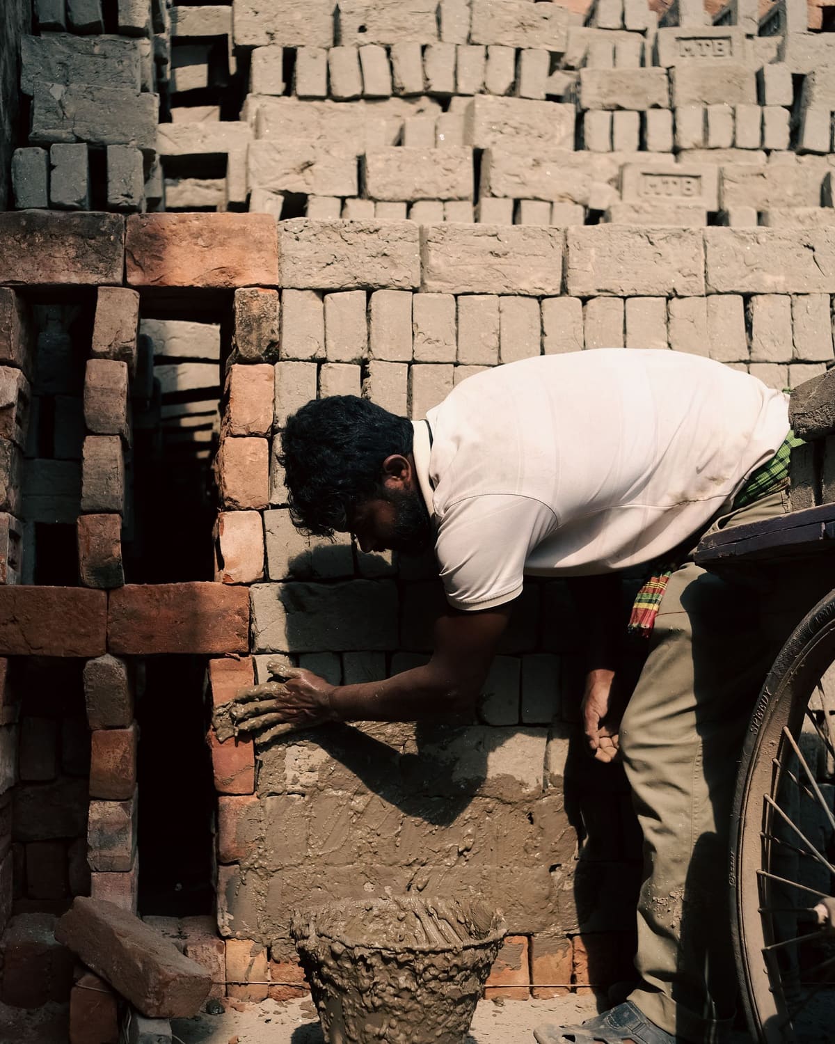 A bricklayer bent over a wall, pressing mortar and setting a brick by hand.