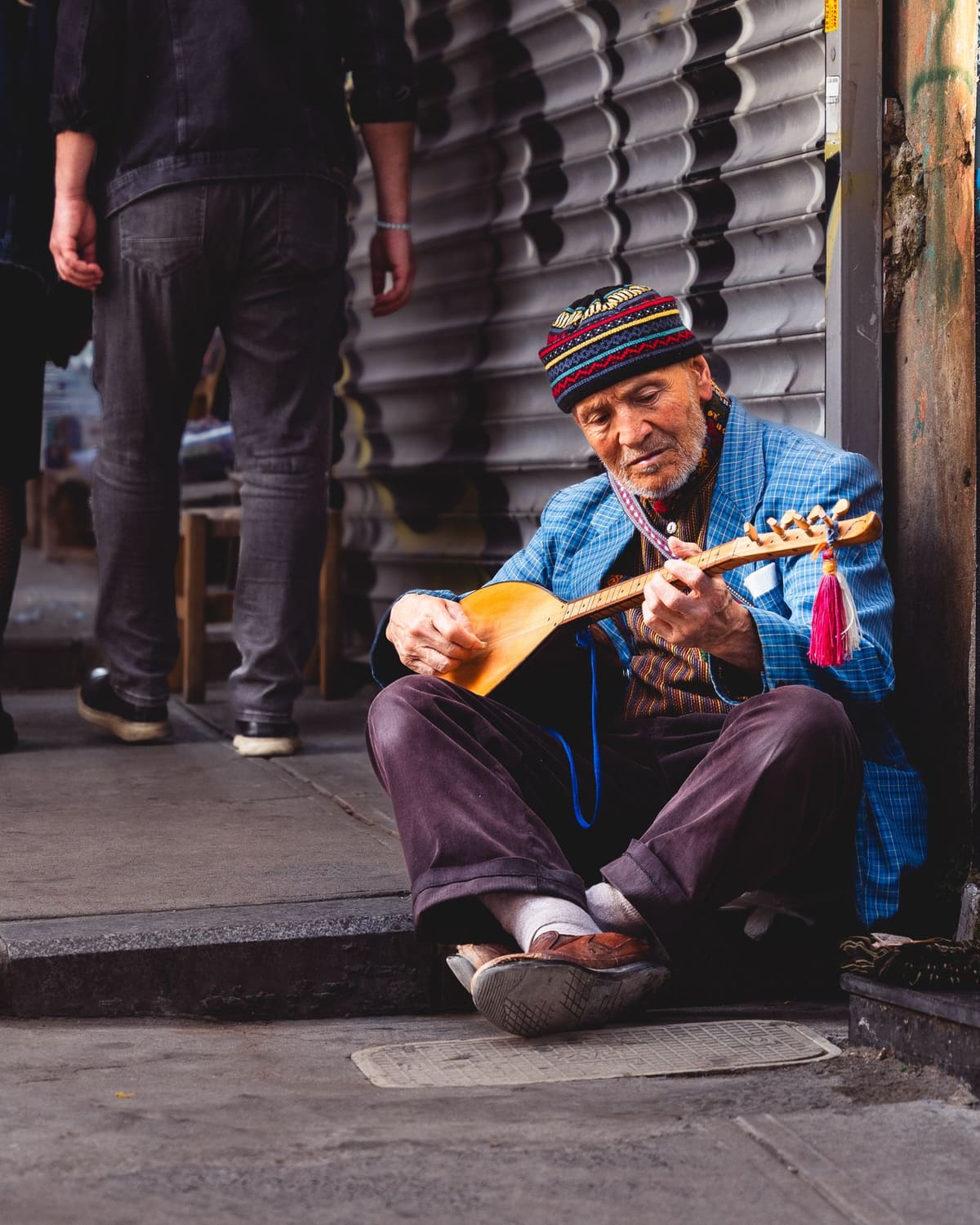 An elderly street musician playing a lute on a city pavement
