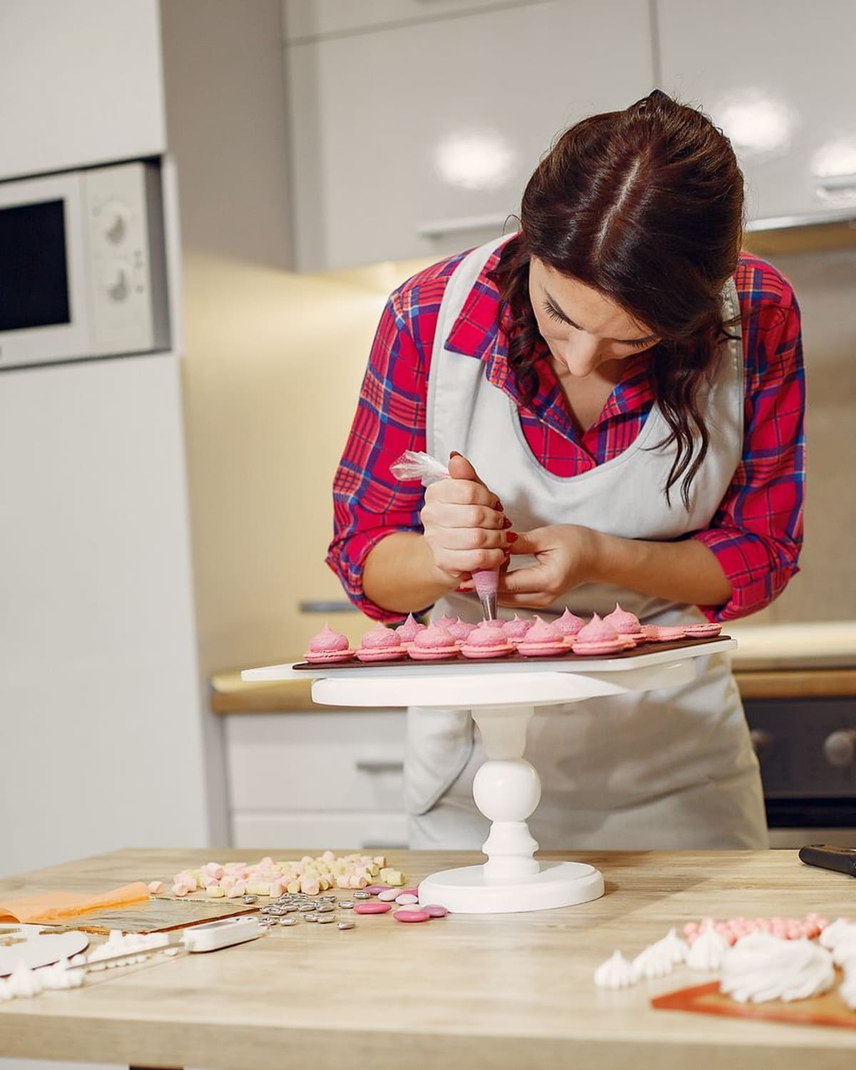 A cake decorator in an apron piping delicate pink decorations onto a cake in a bright kitchen