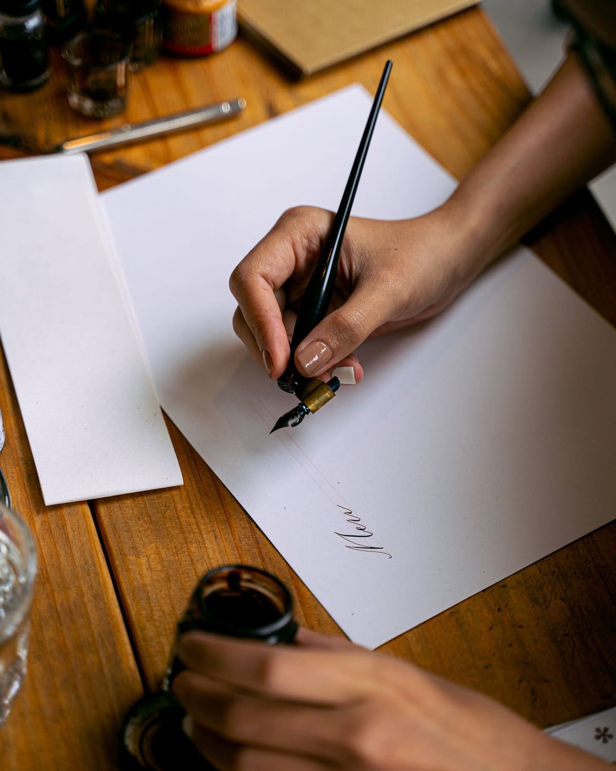 A calligrapher's hand writing script with a dip pen and ink on paper