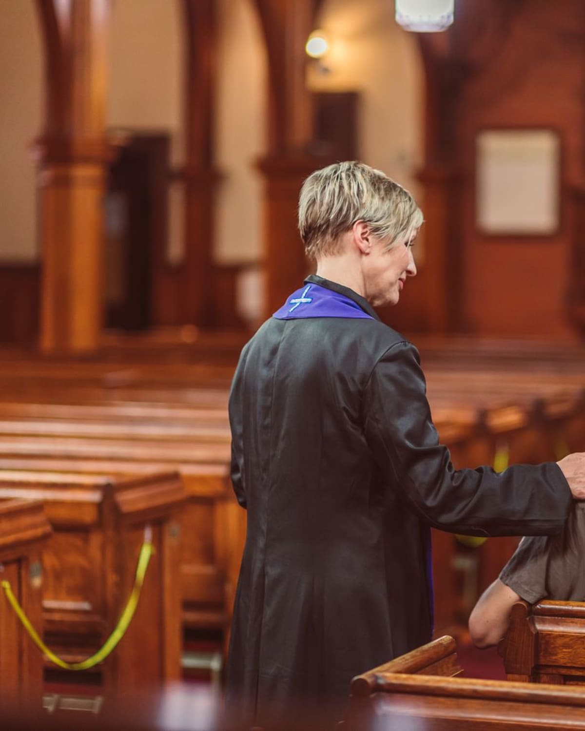 A chaplain in robe and stole resting a hand on a young man's shoulder in a quiet church, talking gently