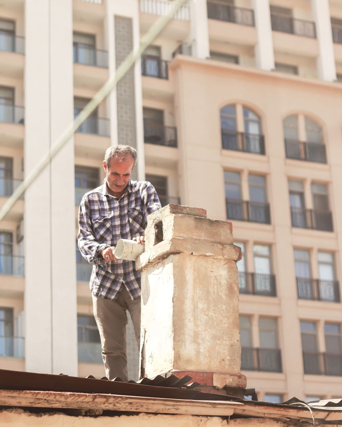 A man on a rooftop working on a brick chimney in warm sunlight.