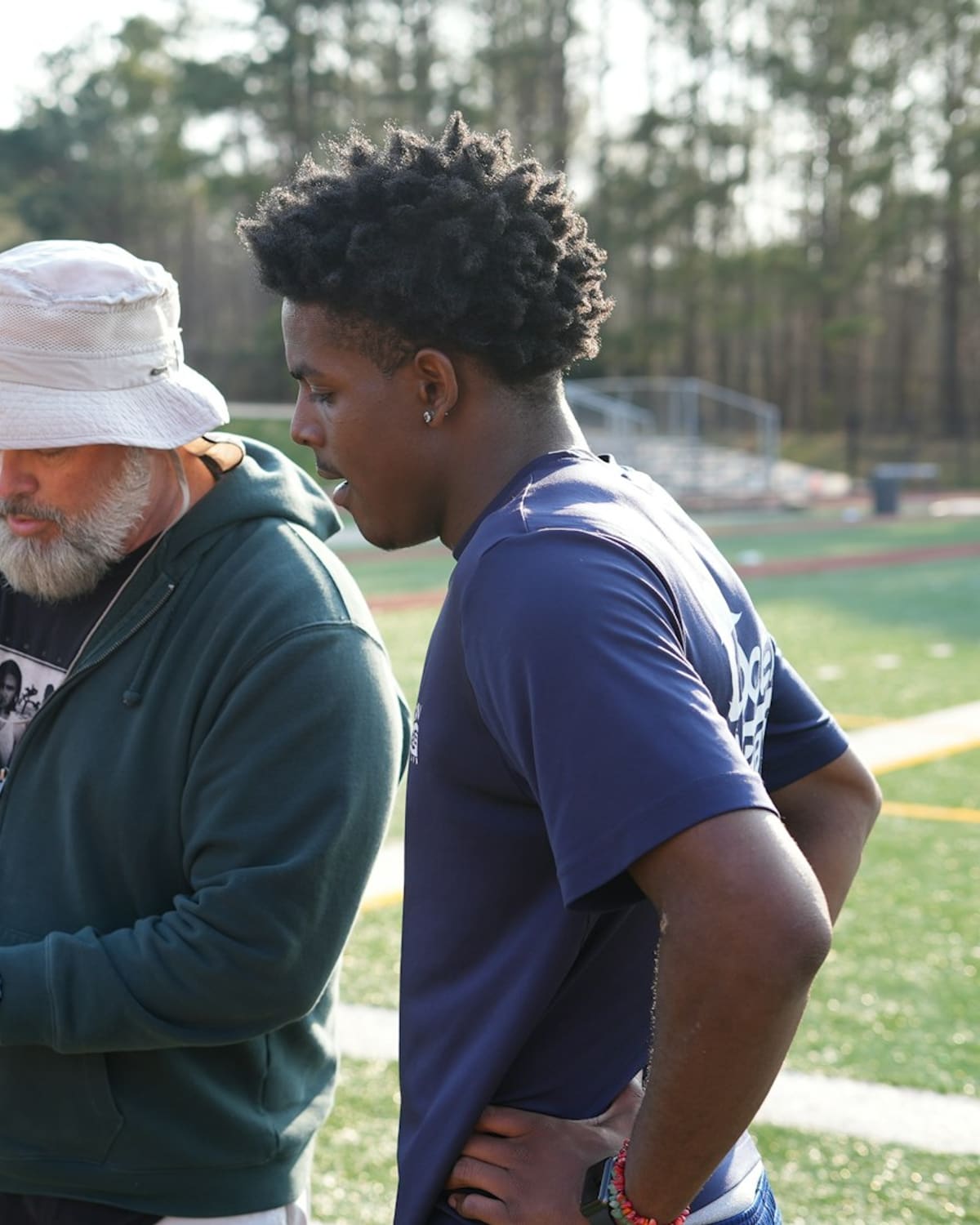 A coach talking one-on-one with a young athlete on a sunlit field