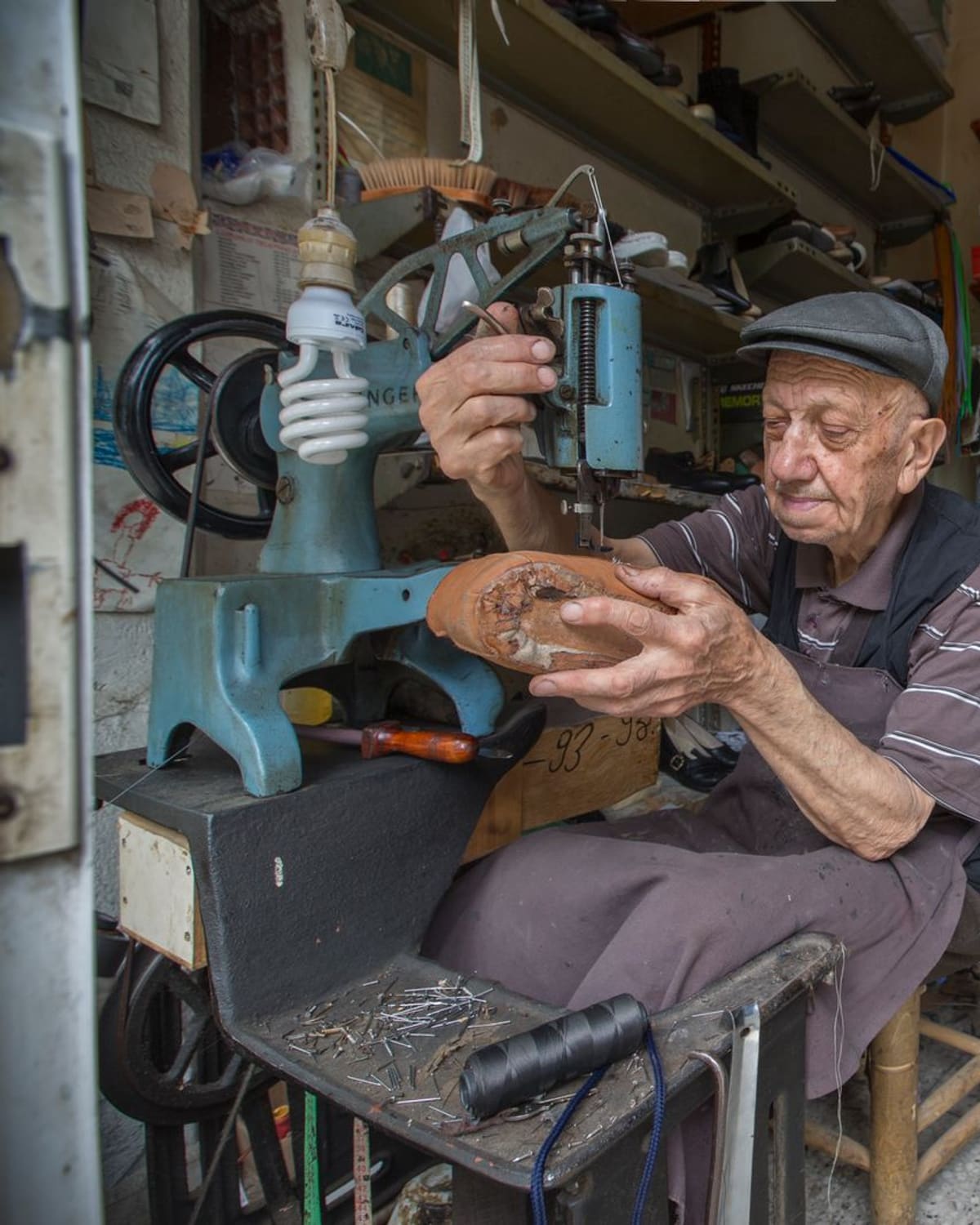 An elderly cobbler at his stitching machine, resoling a worn shoe by hand