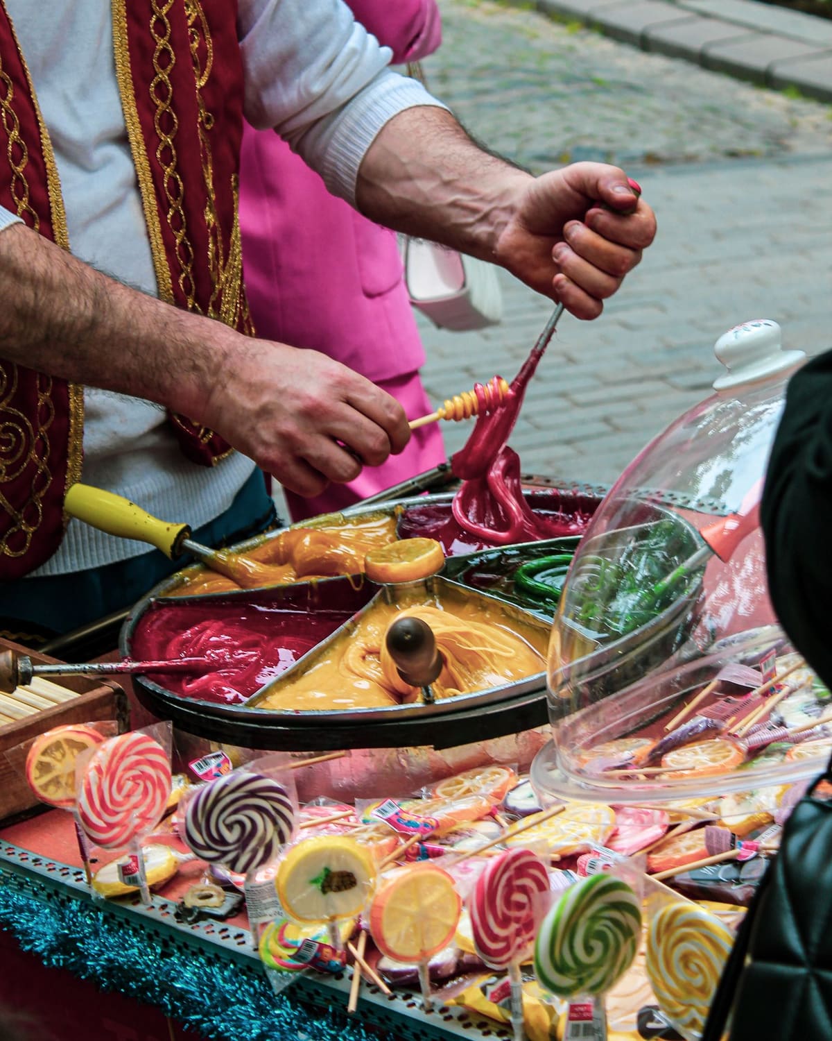 A confectioner pulling and shaping bright molten candy at a market stall, finished lollipops in front