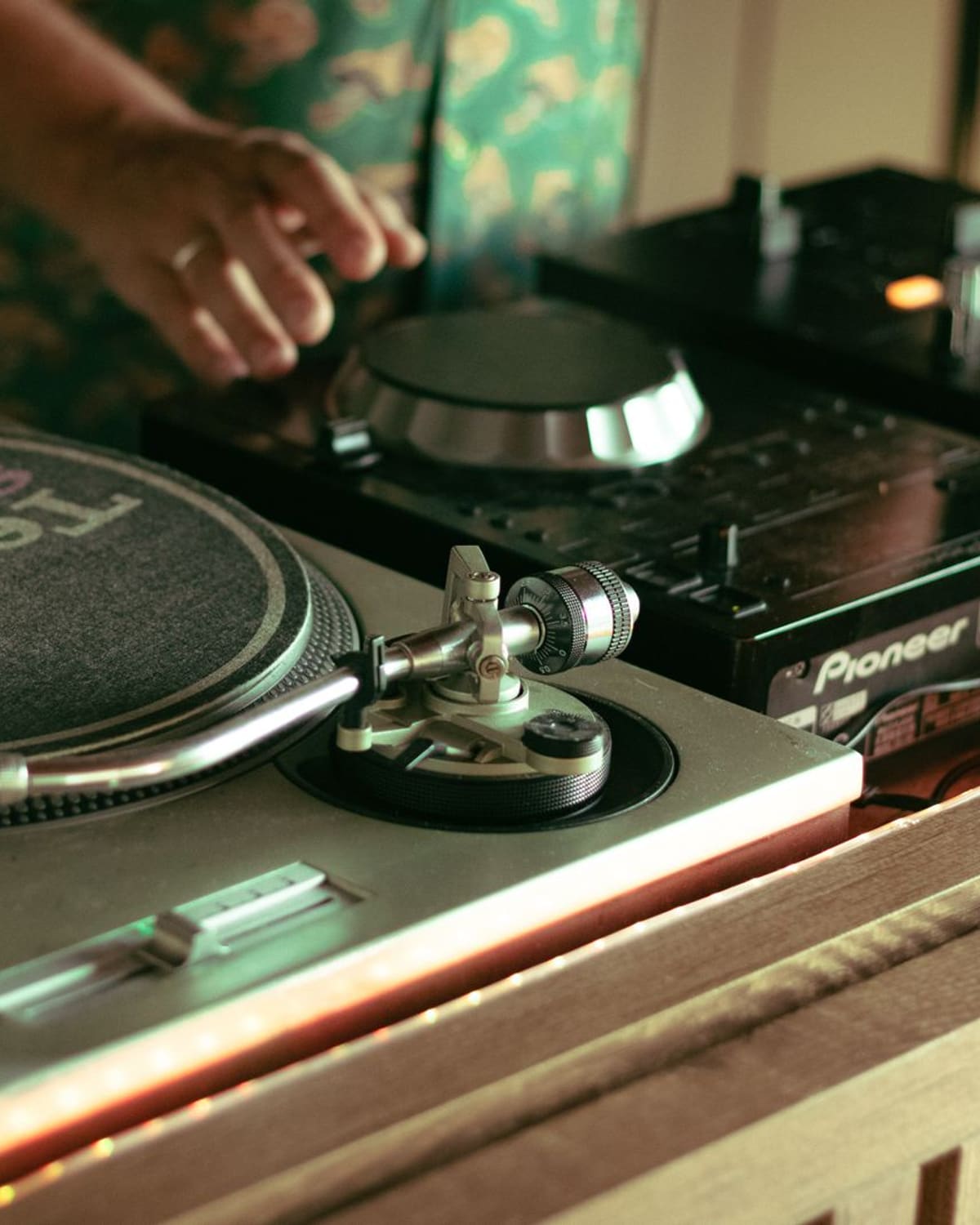 A DJ's hand on the turntable, mixer and vinyl under warm light