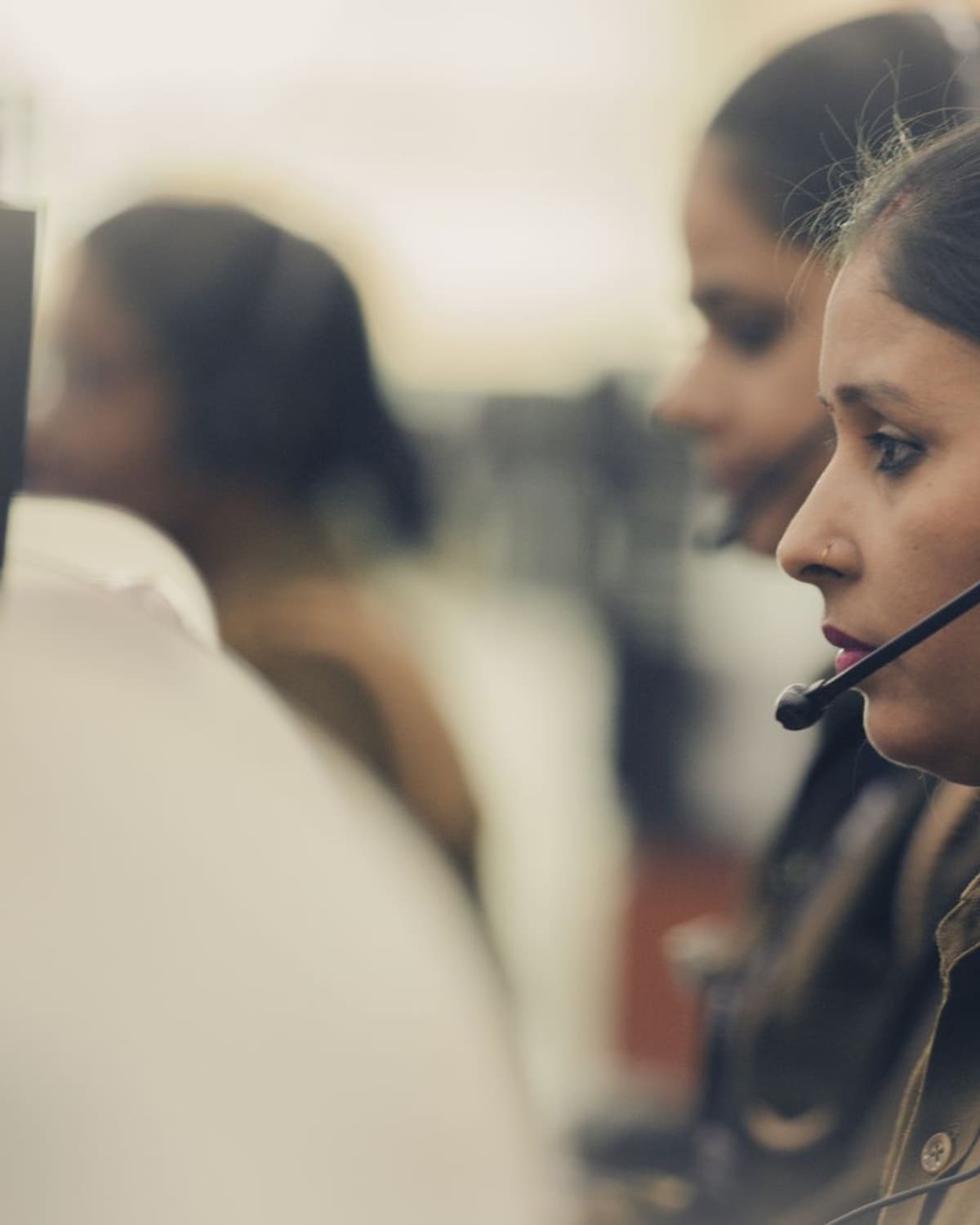 An emergency dispatcher in uniform works the console with a headset, focused on the call.
