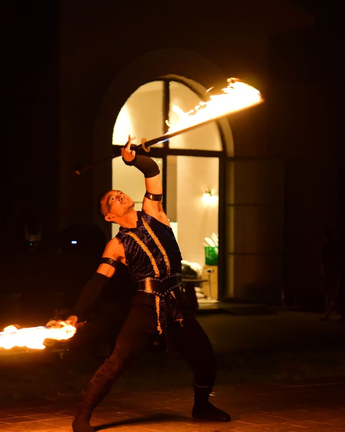 A fire performer spinning flame in the dark before an arched doorway