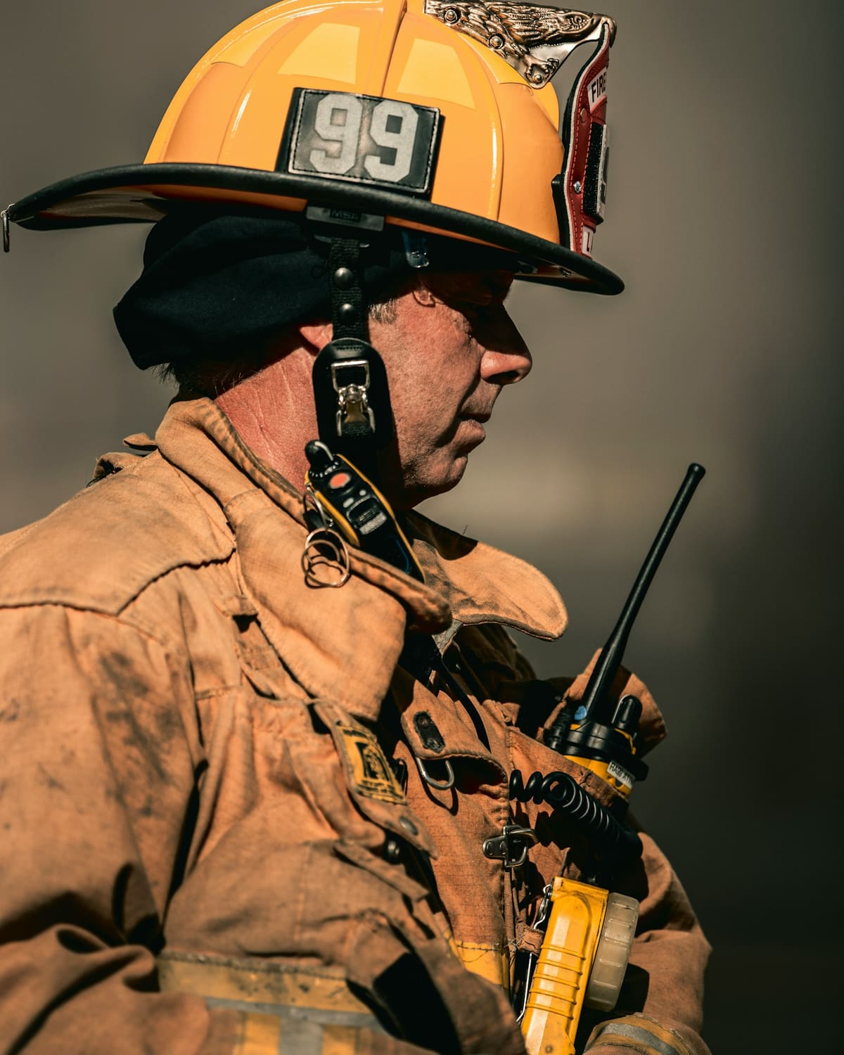 A firefighter in soot-covered gear, radio at hand