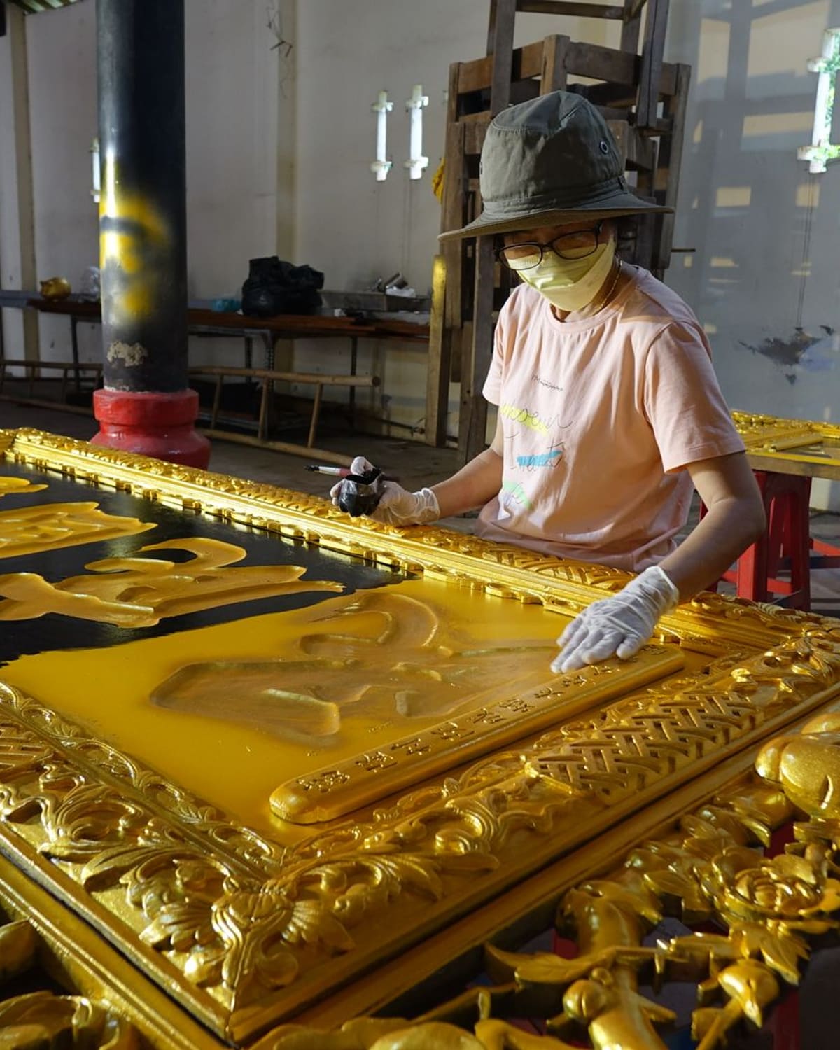 A gilder in gloves applying gold leaf to an ornate carved panel in a bright workshop