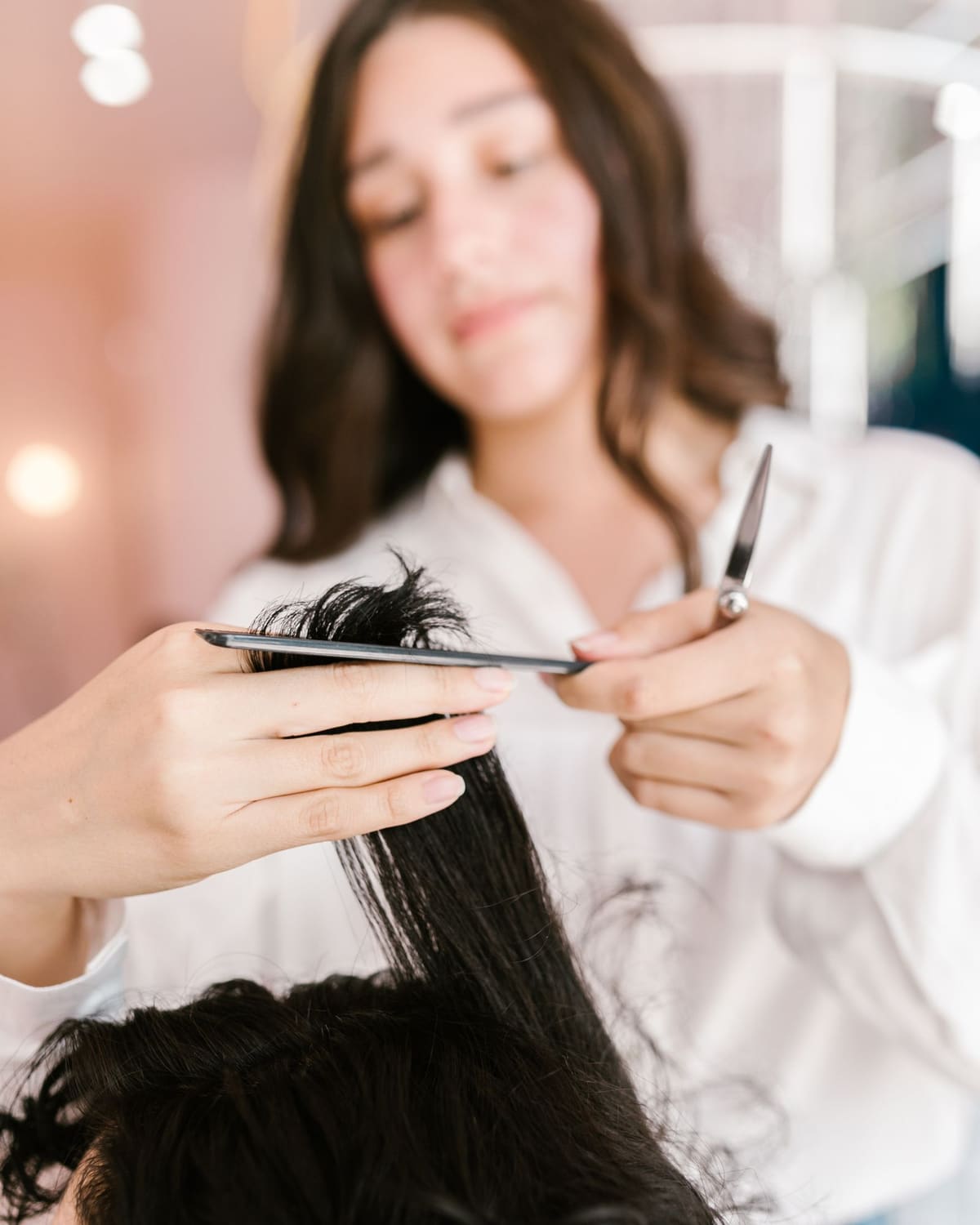 A hairdresser's hands cutting a section of hair in a warm salon