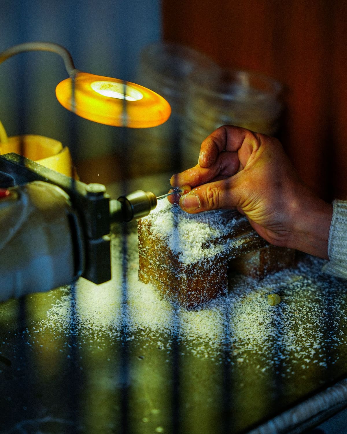 A jeweler's hands working a small piece at the bench under a warm lamp