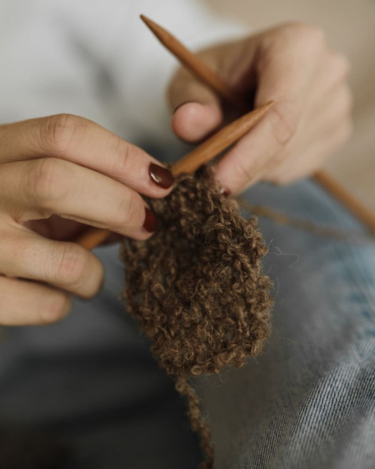 Close-up of a woman's hands knitting brown wool with wooden needles, resting on her lap in soft natural light.
