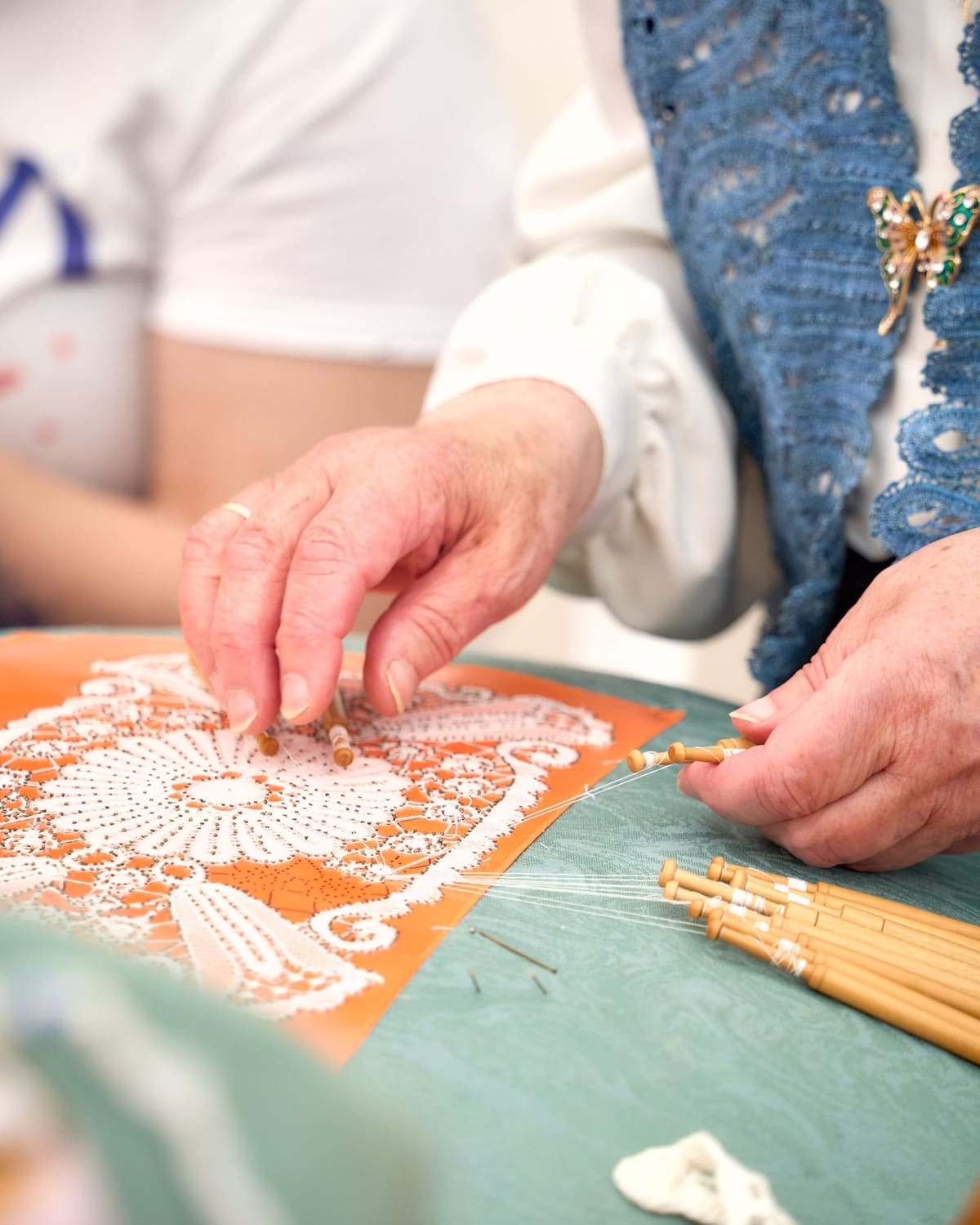 Close-up of a lacemaker's hands working thread across a piece of lace on a pillow.