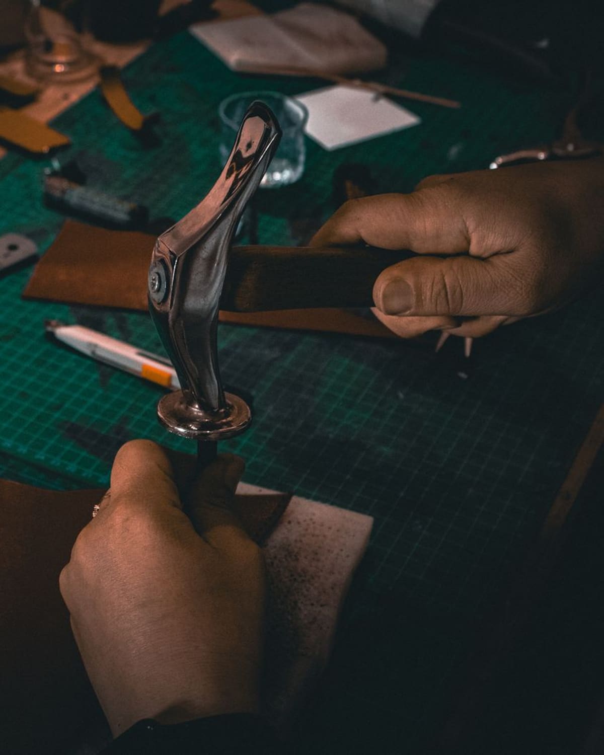 A leatherworker's hands stitching and tooling leather at a workbench