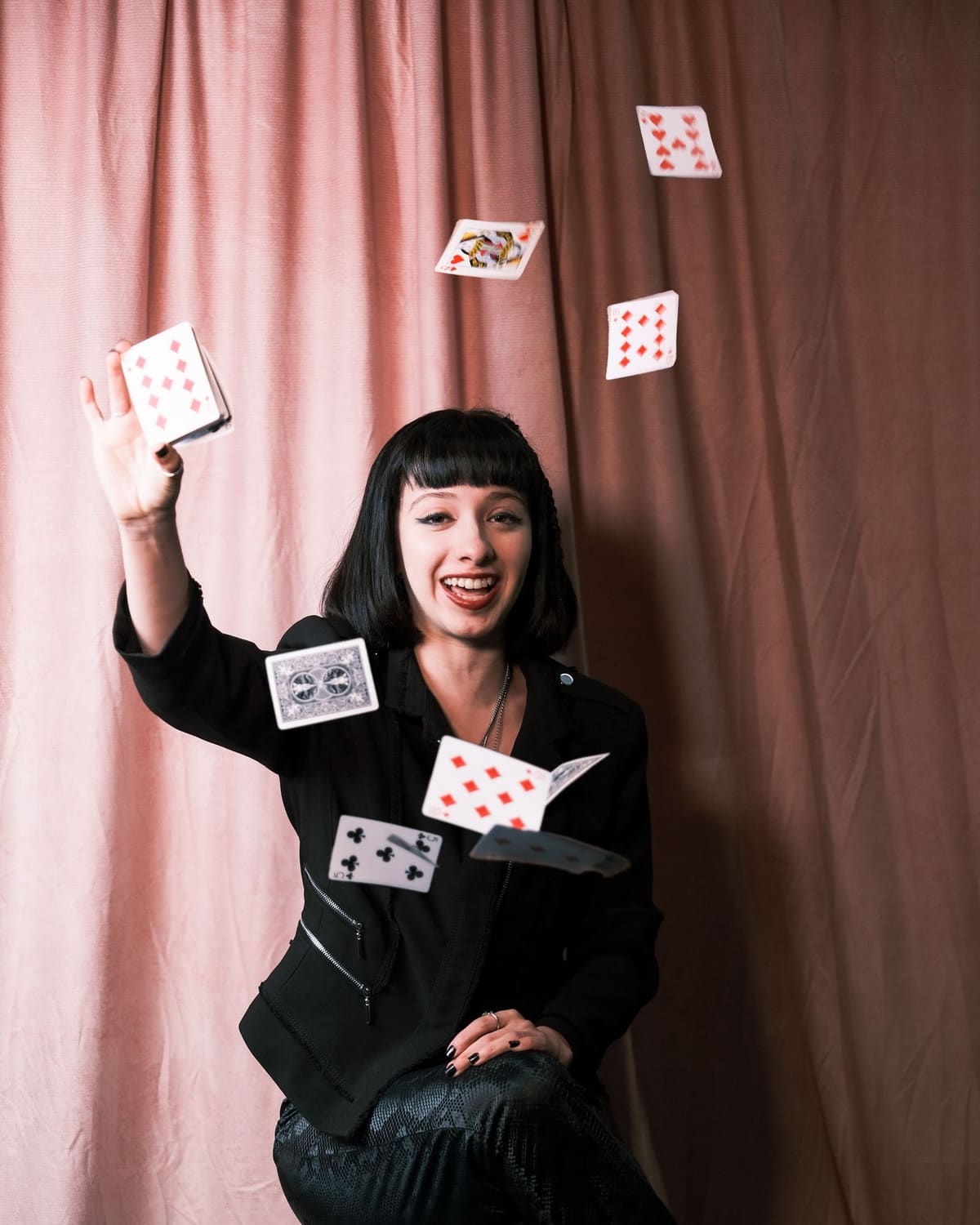 A grinning performer on a stool tossing a spray of playing cards into warm light.