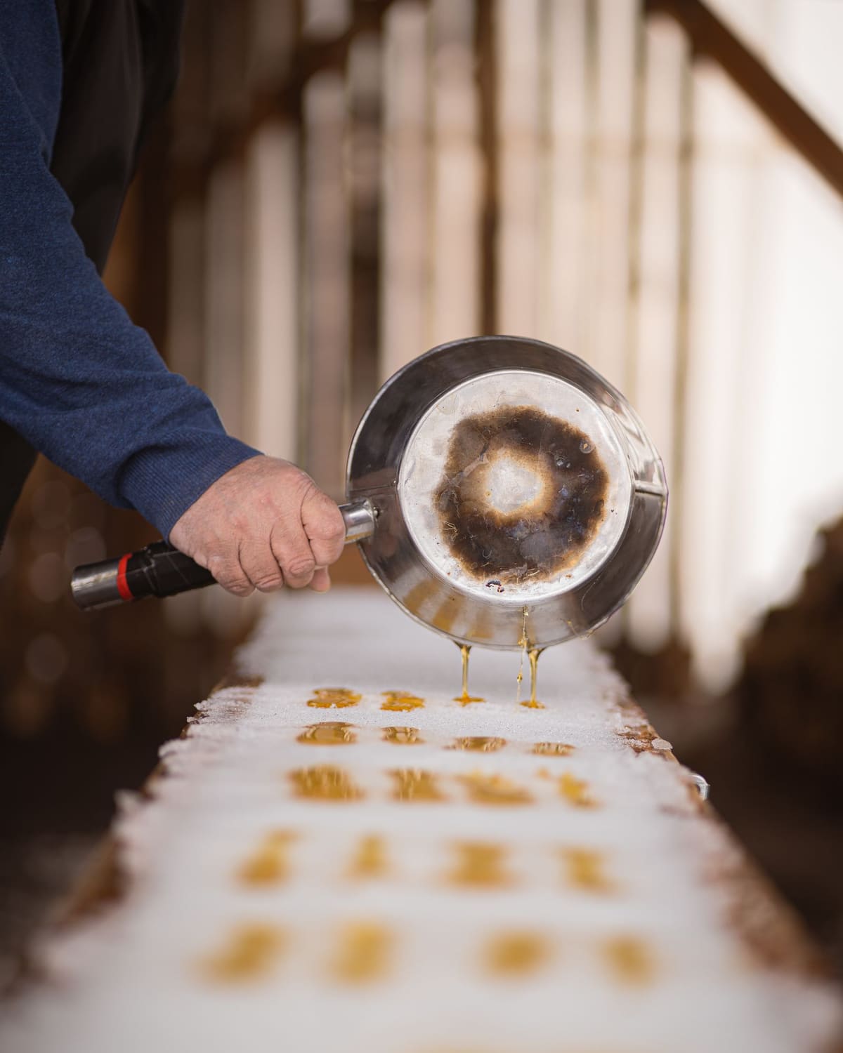 A syrup maker pouring hot maple syrup onto fresh snow to make taffy.