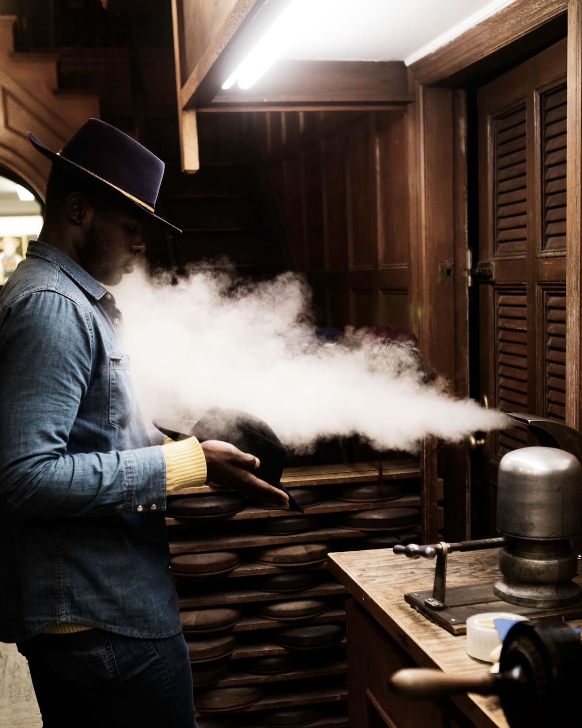 A milliner steaming and shaping a felt hat in a wood-paneled workshop