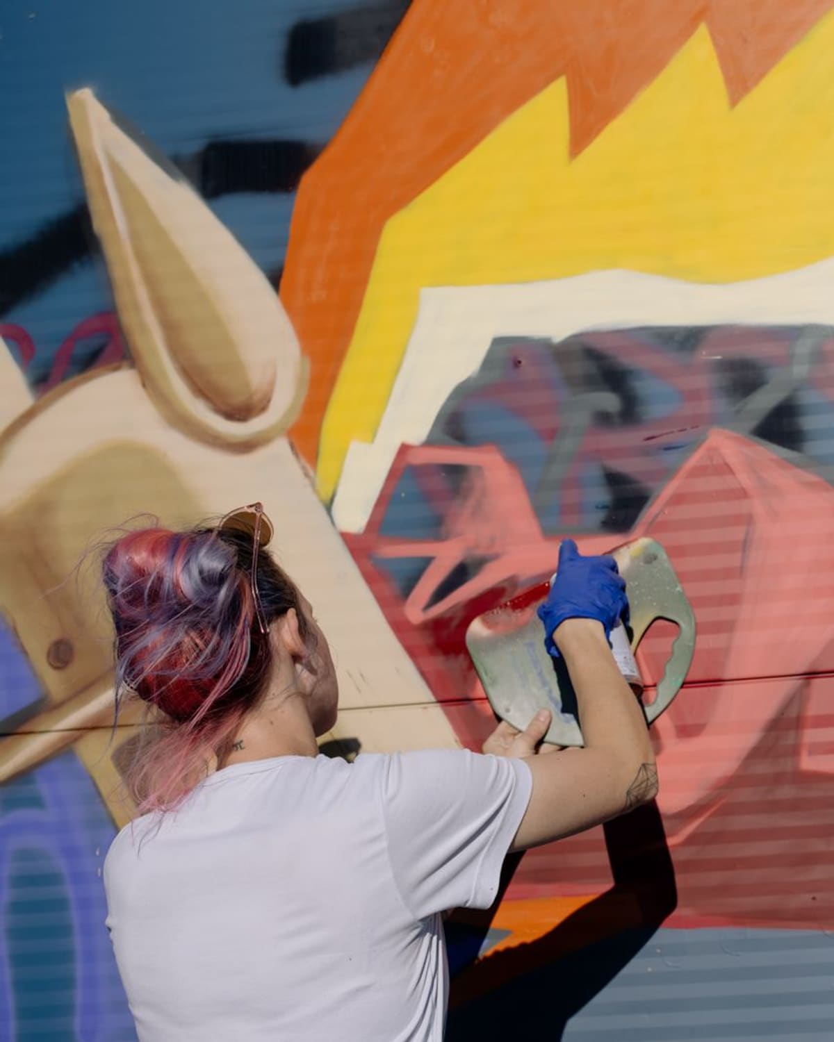A muralist painting a large colorful mural on a public wall