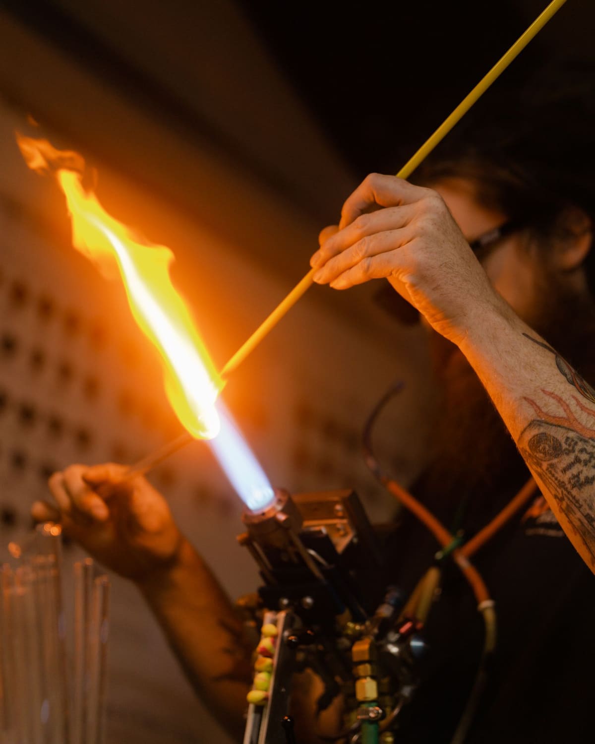 A glassworker heating a glass tube in a torch flame and shaping it by hand in a dim workshop.