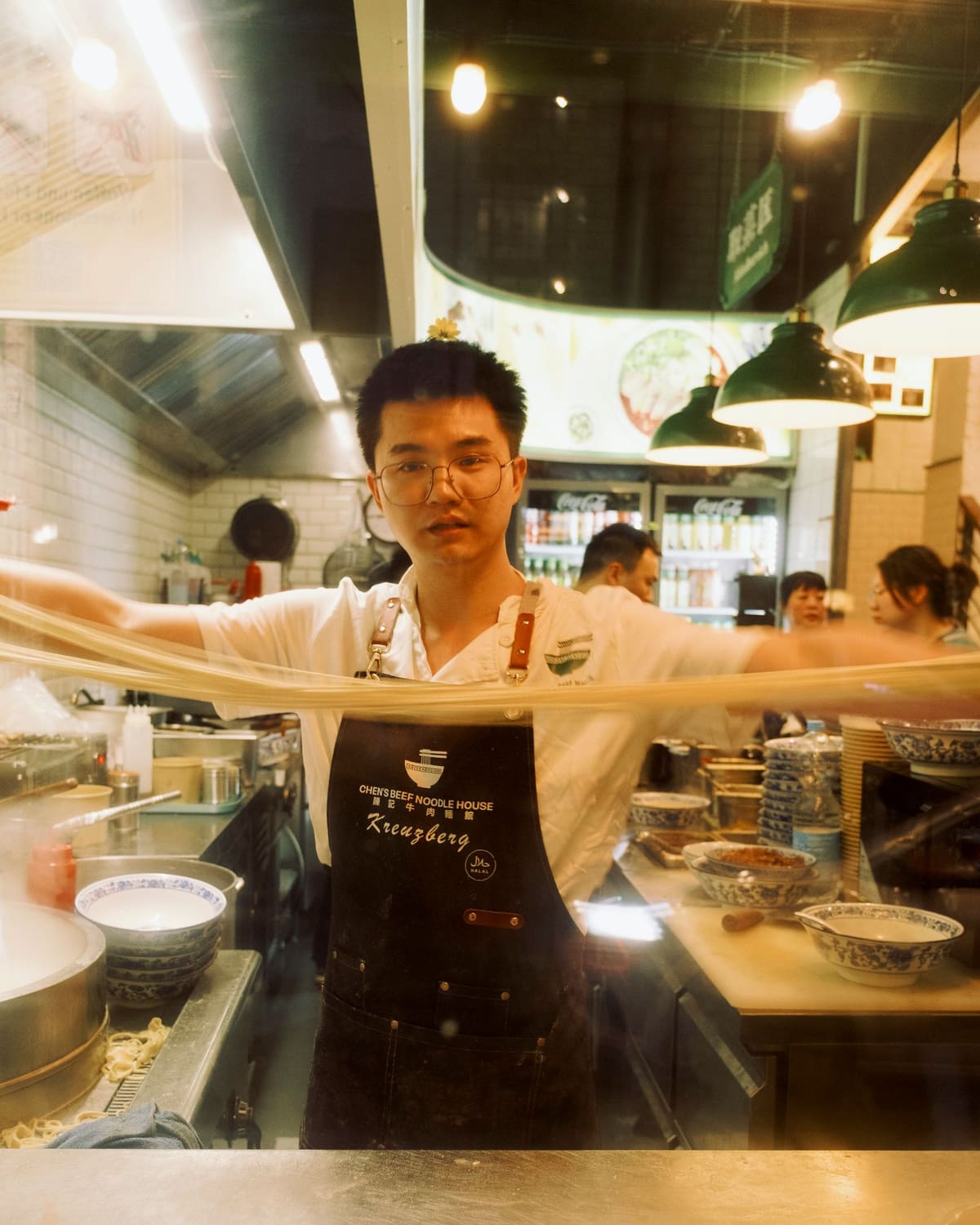 A cook stretching a long loop of hand-pulled noodles in a kitchen.
