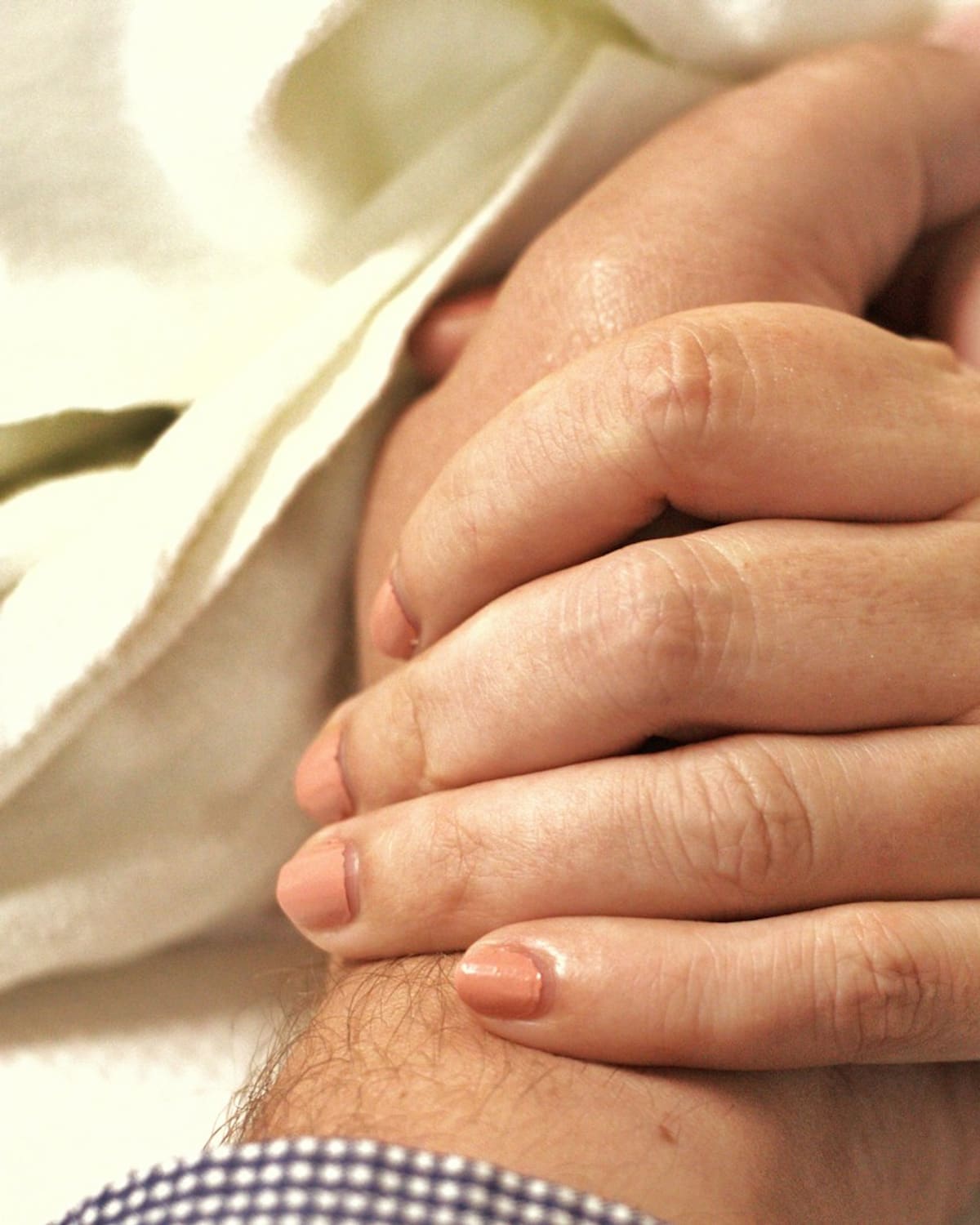 A caregiver's hands clasped over a patient's hand at the bedside