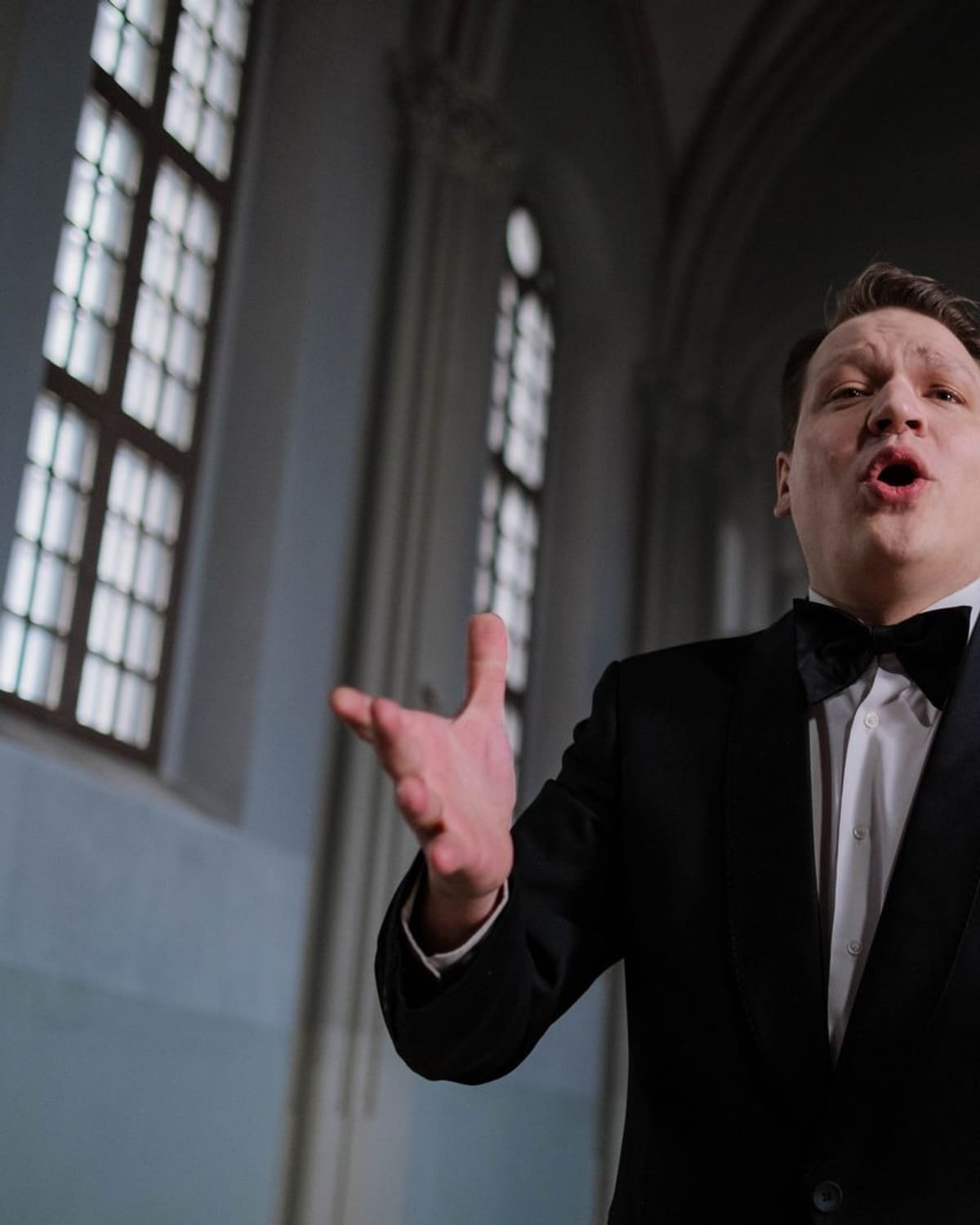 An opera singer in a tuxedo performing a note in a grand hall
