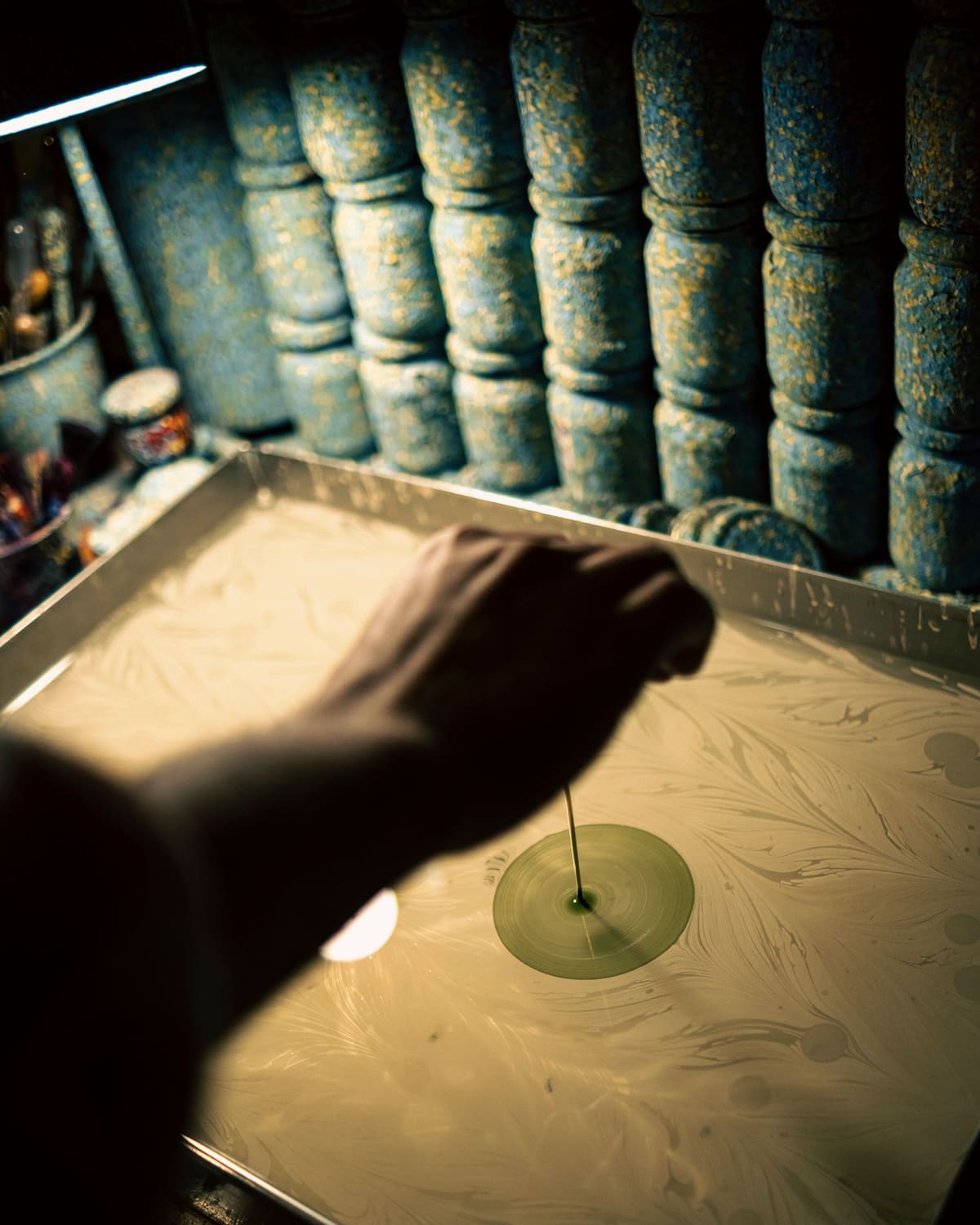 A marbler's hands drawing patterns in floating paint on a water tray with fine styluses