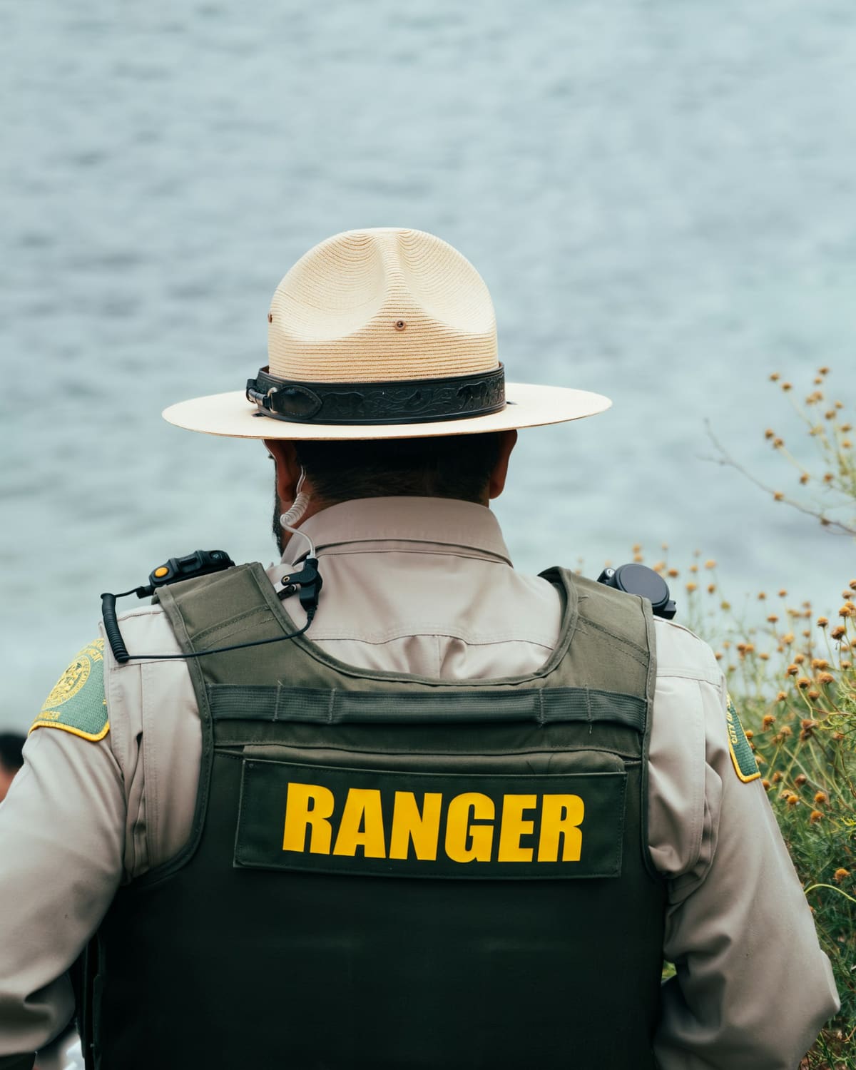 A park ranger in uniform looking out over the water at the edge of a wild place