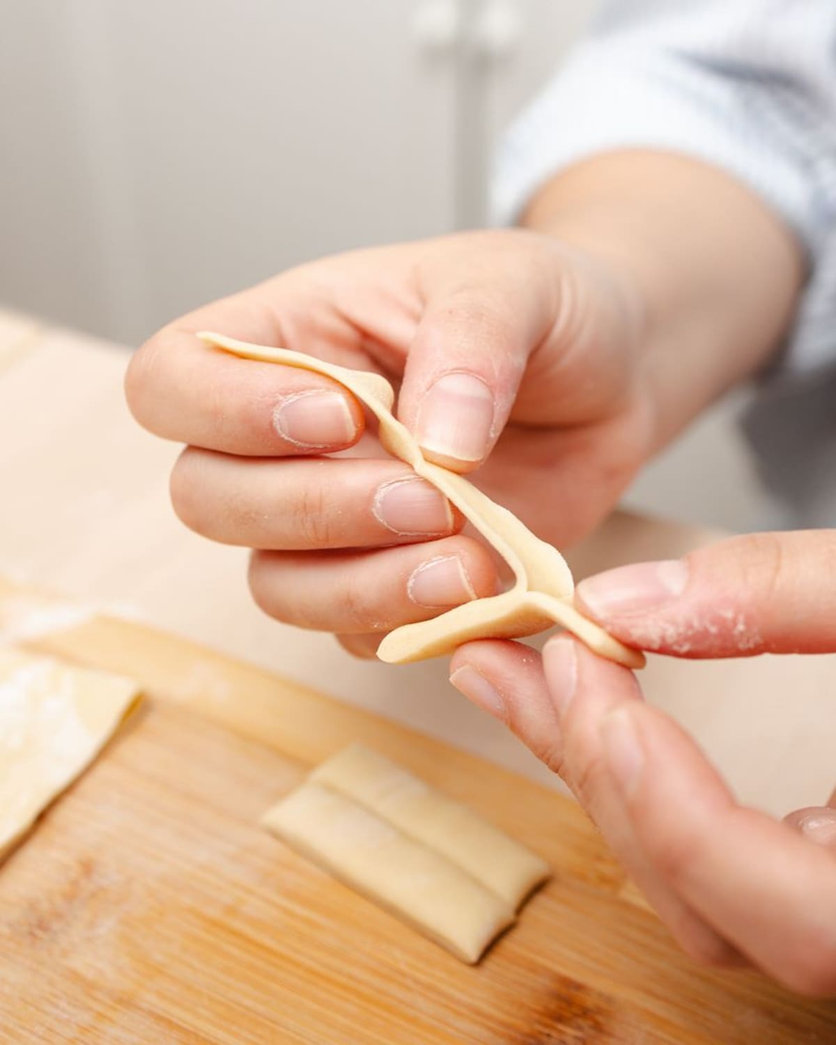 A cook's floured hands shaping fresh egg pasta on a wooden board.