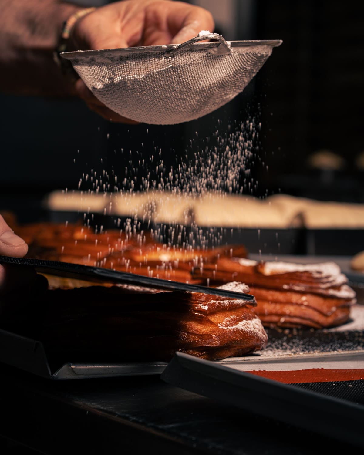 A pastry chef dusting powdered sugar over golden pastries