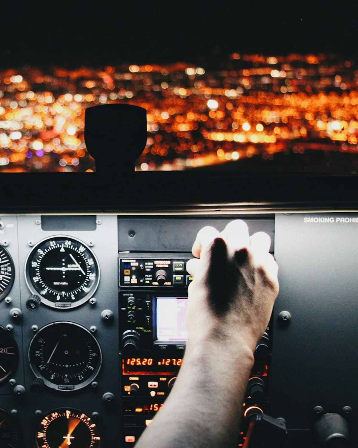A pilot's hand on the cockpit controls, city lights glowing below at night