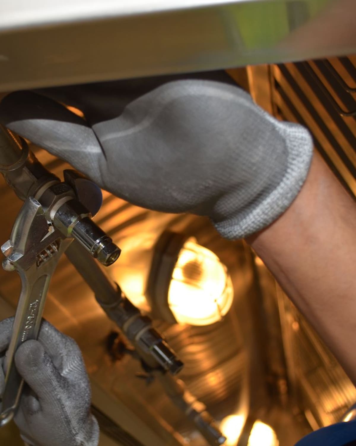 A plumber's gloved hands working a fitting with pliers in warm light