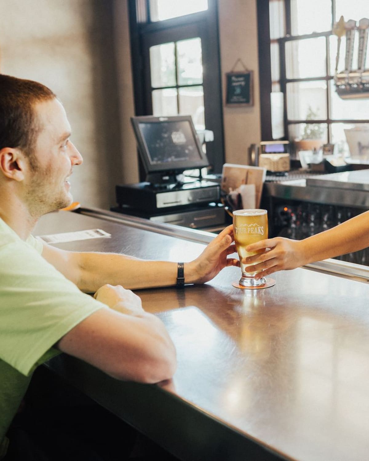 A publican passing a freshly poured pint across the bar to a smiling regular, taps behind her.