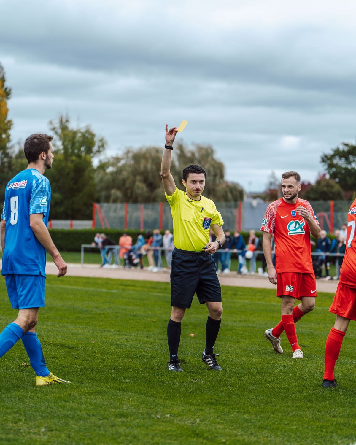 A referee raising a yellow card during an amateur football match