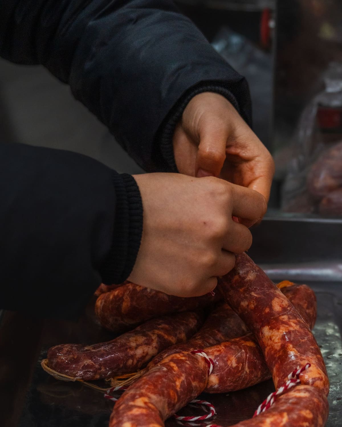 A maker's hands twisting fresh sausages into links on a tray.