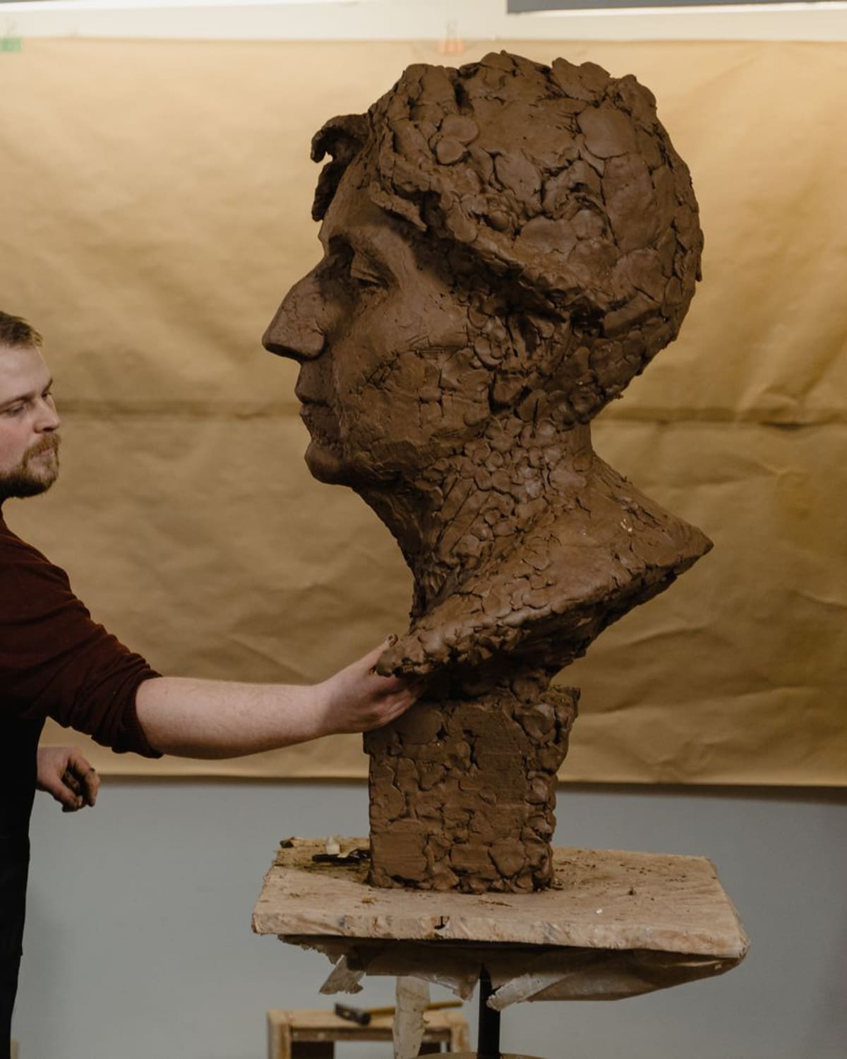 A sculptor shaping a large clay bust in a studio