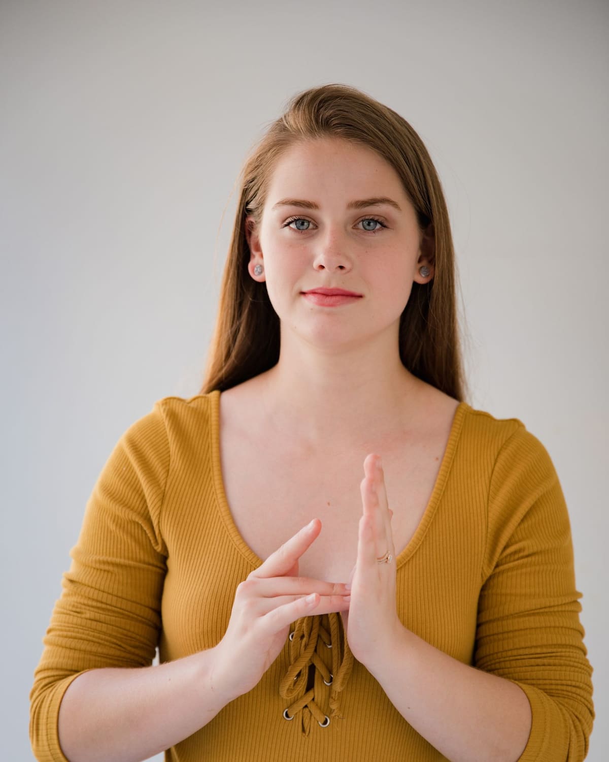 A woman signing with both hands, looking calmly toward the viewer in soft natural light