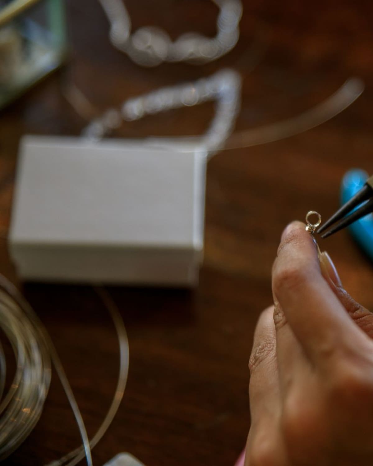 Two hands use pliers to shape a piece of silver wire jewelry on a wooden workbench.