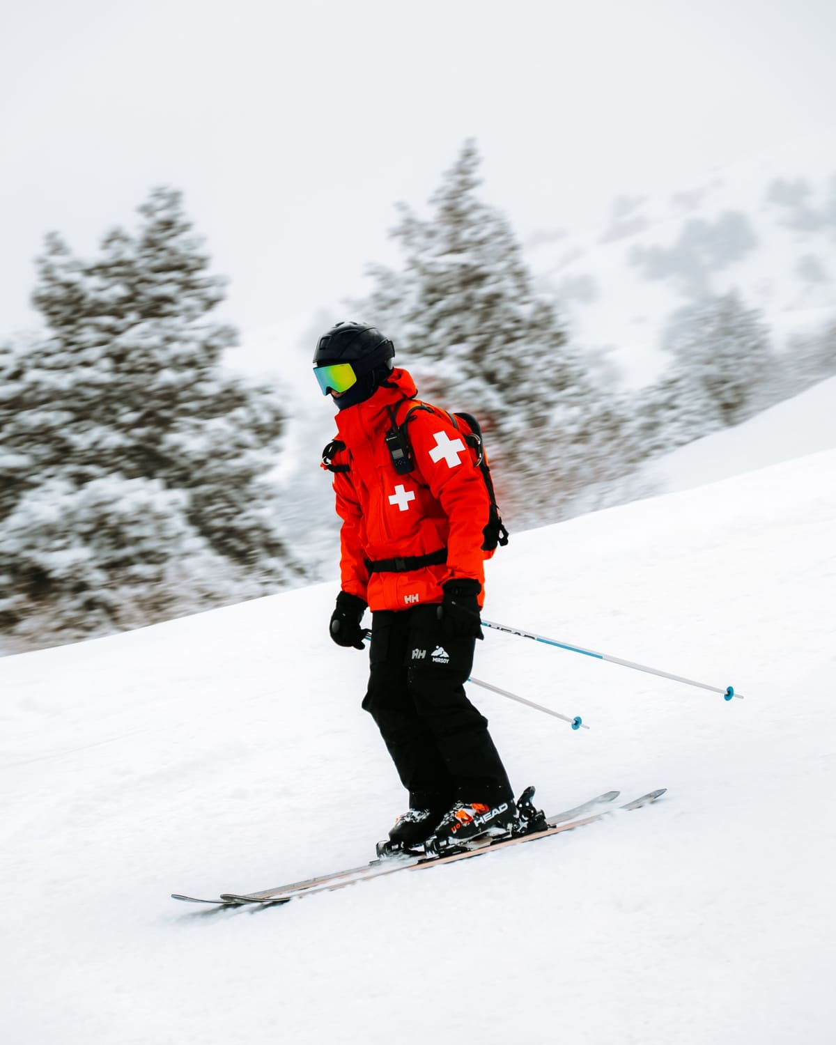 A ski patroller in a red jacket with a white cross skiing down a snowy slope